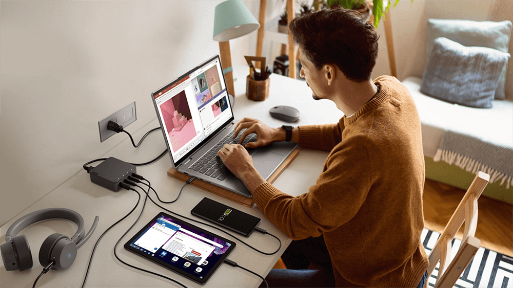 Foto di un professionista in smart working seduto alla sua postazione di lavoro con Notebook, Tablet, Cuffie con microfono e smartphone.
