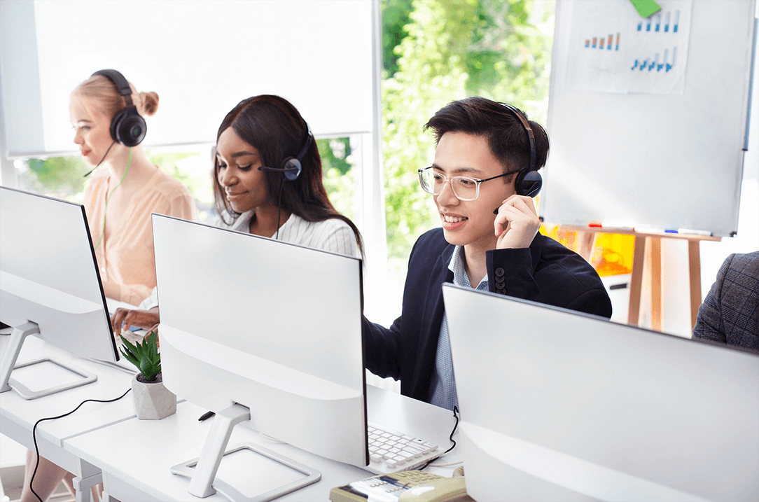 Tre operatori addetti all’assistenza clienti alla postazione di lavoro con monitor, tastiere e cuffie wireless con microfono.