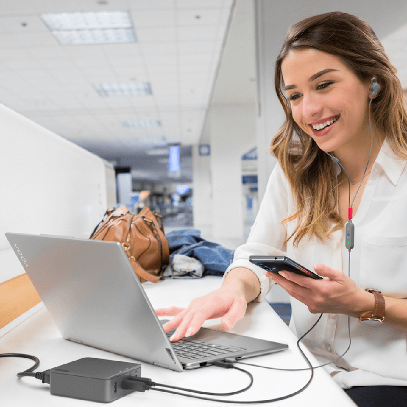 Foto di una donna con in mano uno smartphone mentre utilizza un Notebook e delle cuffie.